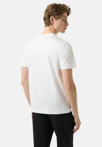 Biały t-shirt z krótkim rękawem i okrągłym dekoltem; miękka tkanina, klasyczny krój oraz gładki wzór; zestawiony z czarnymi spodniami w stylu casual.