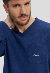 Camiseta de cuello en V de color azul marino en tejido suave, con un pequeño bolsillo en el pecho con logo bordado y mangas texturizadas.