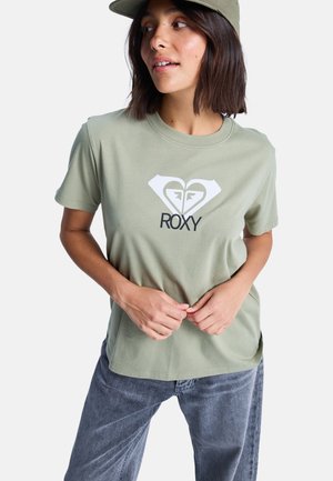 Licht olijfgroen katoenen T-shirt met korte mouwen, voorzien van een witte hart- en logo-print. Gecombineerd met grijze denim broek. Eenvoudig ontwerp.