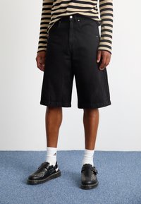 Černé denim šortky s volným střihem, s rovnými nohavicemi a předními kapsami. Nosené s bílými ponožkami a černými botami s dekorativními akcenty.