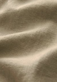 Tissu beige avec un tissage texturé, affichant de légères rides et des variations de ton et de texture naturelles et subtiles.