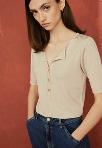 Beige ribbet kortærmet top med en klippestudser og knaplukning, parret med højtaljede blå denim jeans.