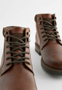 Bruine leren enkelboots met ronde neuzen, voorzien van metalen oogjes, gestructureerde bruine veters en een stevige rubberen zool.