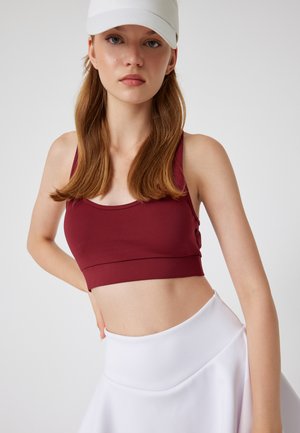 Bordeaux sportsbh med tætsiddende design og brede stropper, parret med en hvid højhalset nederdel med en glat tekstur og udvidet form.