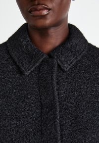 Black textured coat with a collared neckline and button closure. Fabric appears soft and fuzzy, showcasing a close-up of the material.