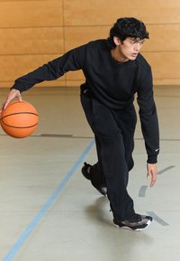Pantalones de chándal y sudadera negra, botando un balón de baloncesto naranja. Tejido texturizado, ajuste atlético, combinados con zapatillas negras y grises.