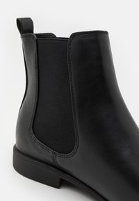 Zwarte leren Chelsea-boot met elastische zijpaneel, gladde textuur en zwarte rubberen zool. Voorzien van een lusje aan de achterkant voor eenvoudig aan- en uittrekken.