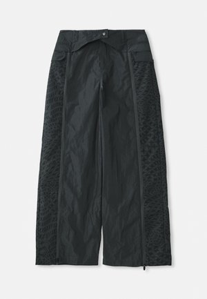 Schwarze weit geschnittene Hosen aus leichtem Material, mit strukturierten Mustern an den Seiten und Reißverschlussöffnungen an den Säumen.