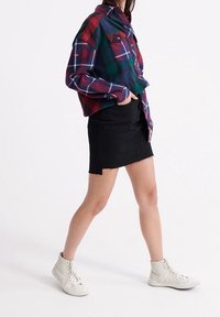 Rutig skjorta i grön, röd och blå med två bröstfickor, kombinerad med en svart denimkjol med fransad nederkant och vita hög-top sneakers.