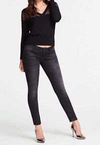 Sweter z akcentem czarnej koronki, V-neck, w połączeniu z ciemnymi dopasowanymi dżinsami i błyszczącymi czarnymi szpilkami. Ma dopasowany krój z lekkim przetarciem.