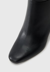 Μαύρη δερμάτινη μποτάκι μέχρι τον αστράγαλο με μυτερή μύτη, λεία υφή και κομψό σχέδιο. Χωρίς ορατά αξεσουάρ ή σχέδια.
