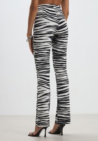 Pantaloni a vita alta con stampa a strisce zebrate bianca e nera, realizzati in un tessuto liscio e elastico. Design a gamba svasata con una silhouette aderente.