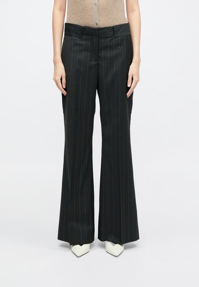 Mustmustriibuline mustad püksid, millel on lai säärekujundus. Omab tasast eesmist vöökohta ja kõrge vöökohaga lõiget. Kombineeritud valgete terava toe kingadega.