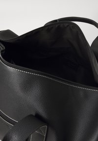 Črna textured usnjena torba s sponko in prostornim notranjostjo. Podloga je iz črne tkanine in ima majhen žep.