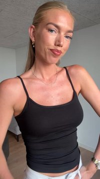 Čierny priliehavý tank top vyrobený z elastického materiálu s tenkými ramienkami, kombinovaný s bielymi džínsami. Jednoduchý dizajn a hladká textúra.