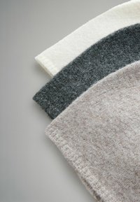 Trzy złożone wełniane koce w kolorach białym, ciemnoszarym i jasnobeżowym, prezentujące miękkie tekstury i subtelny melanżowy wzór.