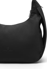 Sac d'épaule Johnny Urban noir avec un détail zippé et une découpe ergonomique de la poignée sur fond blanc.