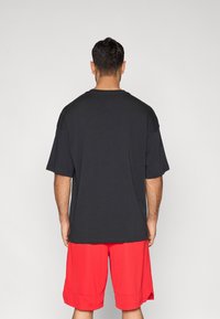 Μαύρο κοντομάνικο μπλουζάκι με στρογγυλή λαιμόκοψη, σε συνδυασμό με κόκκινα αθλητικά σορτς. Το ύφασμα φαίνεται λείο και ελαφρύ.