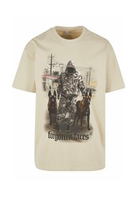 Béžové bavlněné tričko s grafickou ilustrací postavy v kapuci v maskáčovém vzoru se dvěma psy, pod textem je napsáno "zapomenuté tváře."