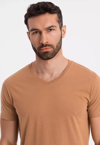 T-shirt a maniche corte e scollo a V in tessuto marrone chiaro. Texture liscia e design aderente, con cuciture sottili lungo il collo.