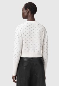 Weißer gestrickter Pullover mit silbernen Sternmustern, verkürztes Design, gerippter Saum und Bündchen, kombiniert mit einem schwarzen Lederskirt mit aufgesetzten Taschen.