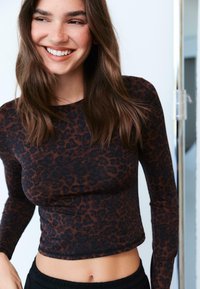 Dolga majica z leopardjim potiskom v rjavi barvi, izdelana iz gladkega, elastičnega materiala; skrajšana zasnova z okroglim izrezom in subtilnimi šivi.