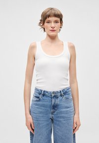 Λευκό βαμβακερό �τοπ χωρίς μανίκια με στρογγυλή λαιμόκοψη, συνδυασμένο με ανοιχτόχρωμο τζιν ψηλόμεσο παντελόνι με κουμπιά μπροστά.