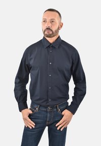Camicia blu navy con colletto, maniche lunghe e vestibilità slim, abbinata a jeans in denim scuro con dettagli di cucitura a contrasto.