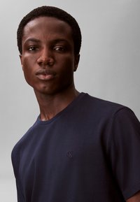 Navyblå t-shirt lavet af blød bomuld, med rund halsudskæring og et lille præget logo på brystet, glat tekstur og enkelt design.