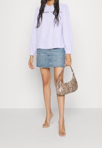 Blusa a maniche lunghe lavanda con dettagli dei bottoni frontalmente, abbinata a una mini gonna di jeans e una borsa a tracolla in pelle di serpente marrone a fantasia. Sandali con tacco trasparente.