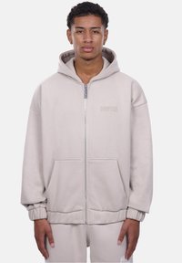 Lys grå zip-up hoodie med en stor hætte, forlommer, ribbede manchetter og et præget brandlogo. Fremstillet af blødt, tekstureret stof.