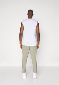 White sleeveless shirt, light khaki tapered pants, white sneakers. Smooth fabric, relaxed fit, minimal design, and no visible patterns.