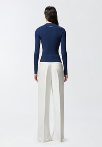 Mornarsko plava rebrasta majica dugih rukava s uskim krojem, uparen s bijelim hlačama visokog struka s detaljem gumba na stražnjem dijelu.