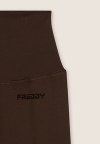 Leggings marroni elasticizzati a vita alta con texture a costine, dotati di un logo nero "FREDDY" in basso a sinistra. Le cuciture sono ordinate e pulite.