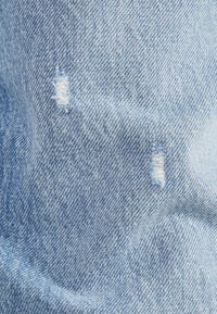 Tela de mezclilla azul claro con dos pequeños desgastes que muestran hilos blancos, destacando la textura gastada y un estilo casual.