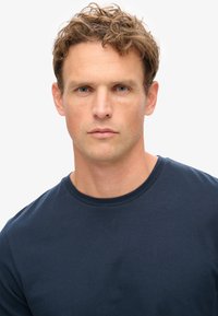 Camiseta de algodón azul marino con cuello redondo y mangas cortas. La tela parece suave, con textura mínima y sin patrones.