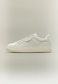 Hvid sneaker med en glat læderoverdel, rund snude og diskret præget logo. Har tonede snørebånd og en gummisål.