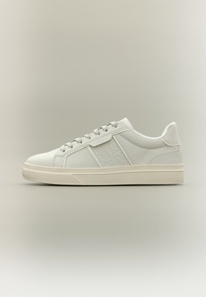 White sneaker with a smooth leather upper, round toe, and subtle embossed logo detail. Features tonal laces and a rubber sole.