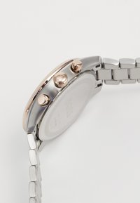 Orologio in acciaio inox argento con una lunetta in oro rosa, tre pulsanti sul lato e un bracciale in metallo a maglie. Retro semplice con branding.