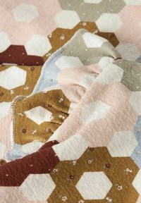 Riešutinis pledas su šešiakampiu raštu pastelinėmis spalvomis: rožine, smėlio spalva, ruda, su gėlių akcentais. Minkštas audinys ir sulankstyti kraštai.