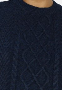 Marineblau gestrickter Pullover mit strukturiertem Kabelmuster, geripptem Kragen und feinem Garn für ein sanftes, glattes Erscheinungsbild.
