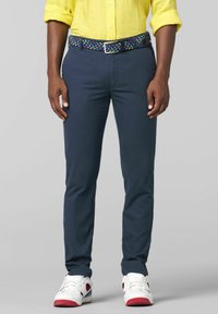 Navy Slim-Fit-Hosen aus Baumwollmischung, kombiniert mit einem mehrfarbigen gewebten Gürtel und weißen Sneakers mit roten Akzenten. Gelbes Hemd sichtbar.