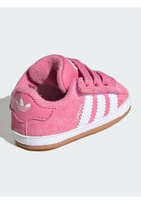 Růžové semišové tenisky s bílými koženými pruhy, zaoblenou špičkou a texturovanou podrážkou. Obsahují logo na patě a polstrovaný, měkký interiér.