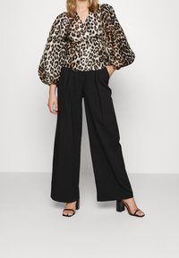 Blouse en soie à imprimé léopard avec manches volumineuses, associée à un pantalon noir taille haute à jambes larges et des sandales noires à talons blocs.