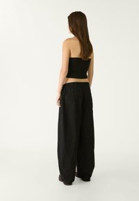 Schwarzes Outfit mit einem enganliegenden trägerlosen Oberteil und lockeren, hoch taillierten Hosen mit elastischem Bund, von hinten gezeigt.