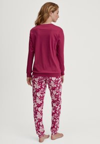 Fuchsia lange mouw top gecombineerd met bloemenpatroon broek met witte bladeren op een roze achtergrond. Zacht materiaal met elastische manchetten.