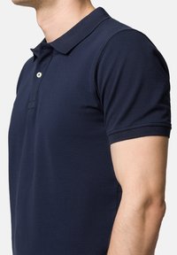 Granatowa koszulka polo z teksturowanej tkaniny, krótki rękaw, klasyczny kołnierzyk oraz zapięcie na dwa guziki. Gładkie wykończenie z mocnym przeszyciem.