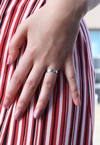 Silver metallic ring on a hand with light skin tone and polished pink nails, touching a vertical striped fabric in red, white, and black.