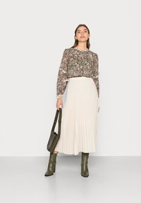 Blusa olive de manga longa com padrão floral e punhos franzidos; saia midi plissada em creme; botas verdes com textura de croco; bolsa a condizer.