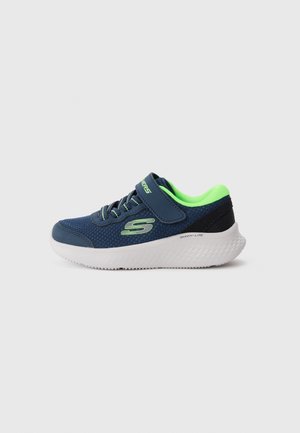 Baskets enfants bleu marine et vert néon avec bride velcro, semelle blanche et logo "S" sur le côté sur fond uni.